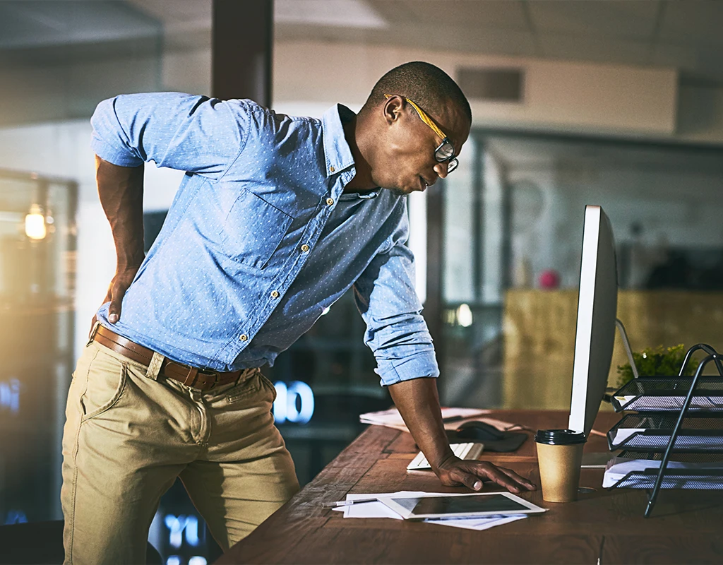 Man Standing At A Desk With Back Pain Over A Computer